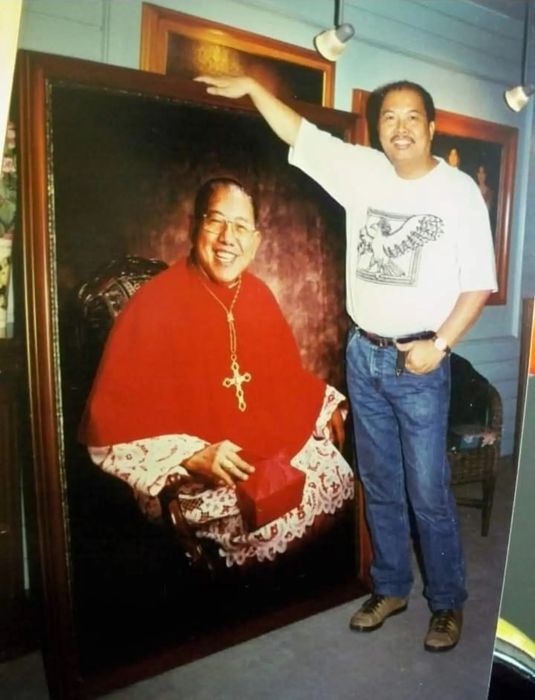 Jorge in the studio, resting a hand on the frame of a life-size portrait he made of a cardinal in full red vestments