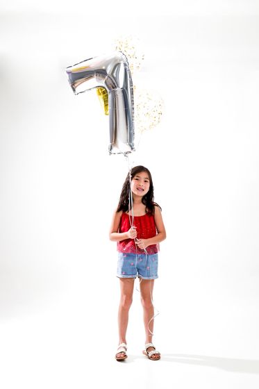 A child standing beneath a silver number balloon on white