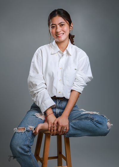 A young woman in a white shirt and jeans seated on a stool