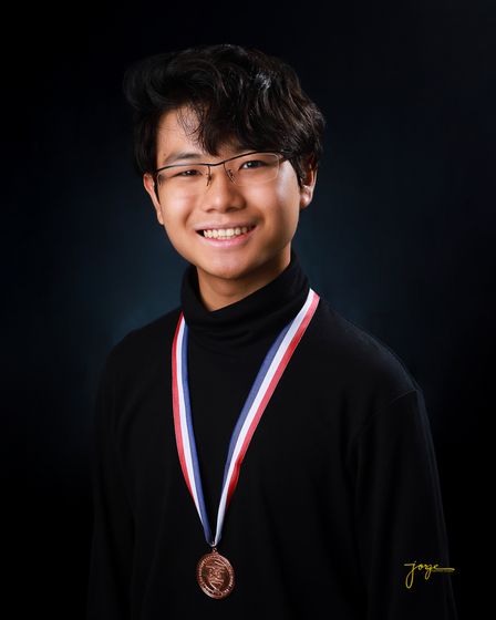 A graduate in a black turtleneck wearing an academic medal