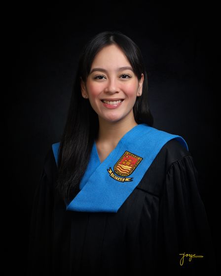 A graduate in cap-and-gown sash smiling against black