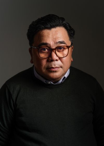 A man in glasses and a dark sweater, lit against a deep grey background