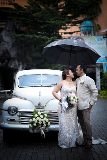 A couple beside a vintage car under an umbrella