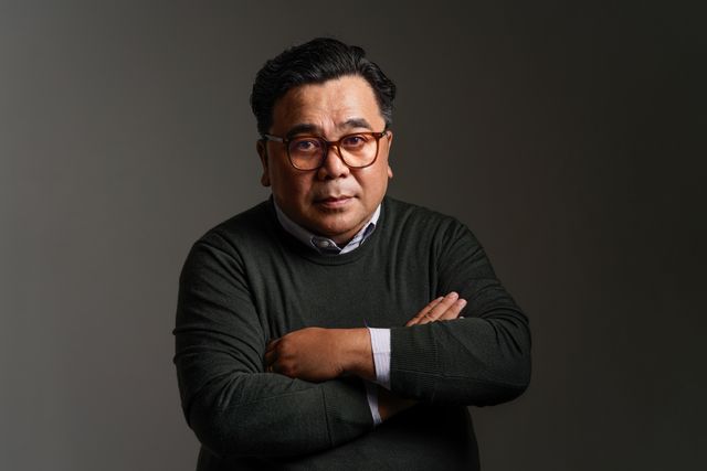 A corporate headshot of a man with folded arms, lit against a grey background